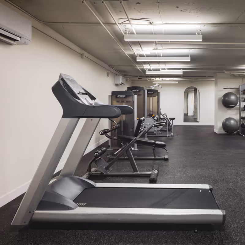 Fitness center with Precor treadmills lined up against white wall, weight machines visible in background on black rubber