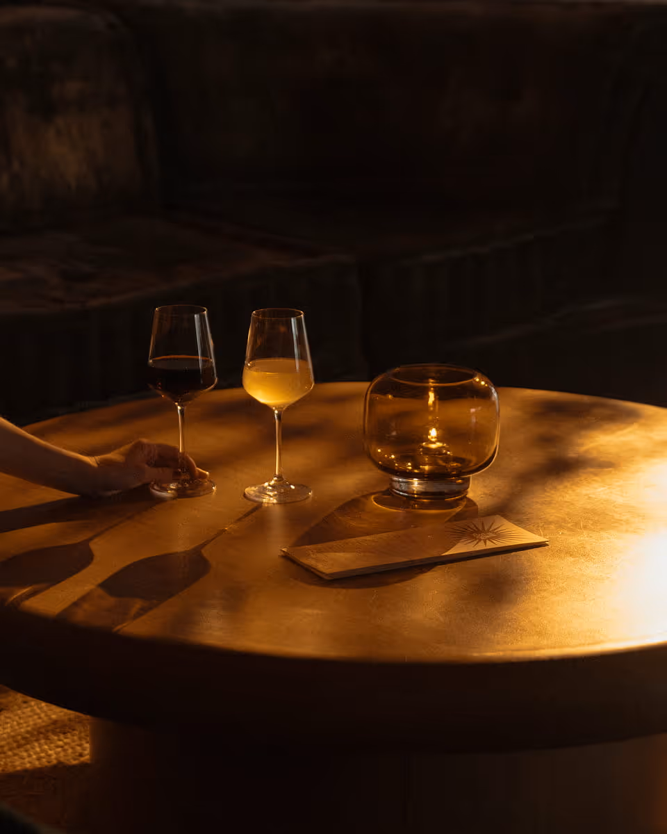 Two wine glasses, one red and one white, on a warm golden round table in a dimly lit lounge with a candle holder