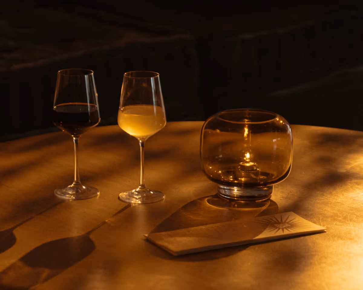 Two wine glasses, one with red and one with white wine, beside an amber glass candle holder on a warmly lit wooden table.
