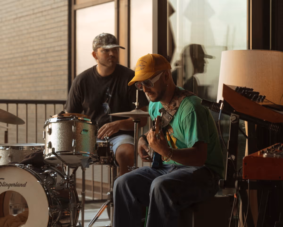 Two musicians jamming together, one playing a Slingerland drum kit and the other playing guitar in a warm studio setting.