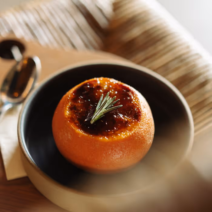 Brûléed grapefruit half garnished with a fresh rosemary sprig, served in a dark ceramic bowl on a sunlit table