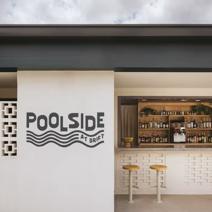Poolside at Drift outdoor bar featuring retro signage, decorative breeze block walls, wooden bar stools, and a fully stocked