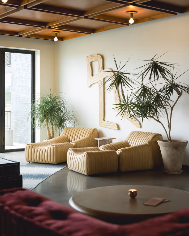 Modern hotel lobby lounge with tan channeled leather sofas, tropical plants, abstract wall sculpture, and a wooden coffered