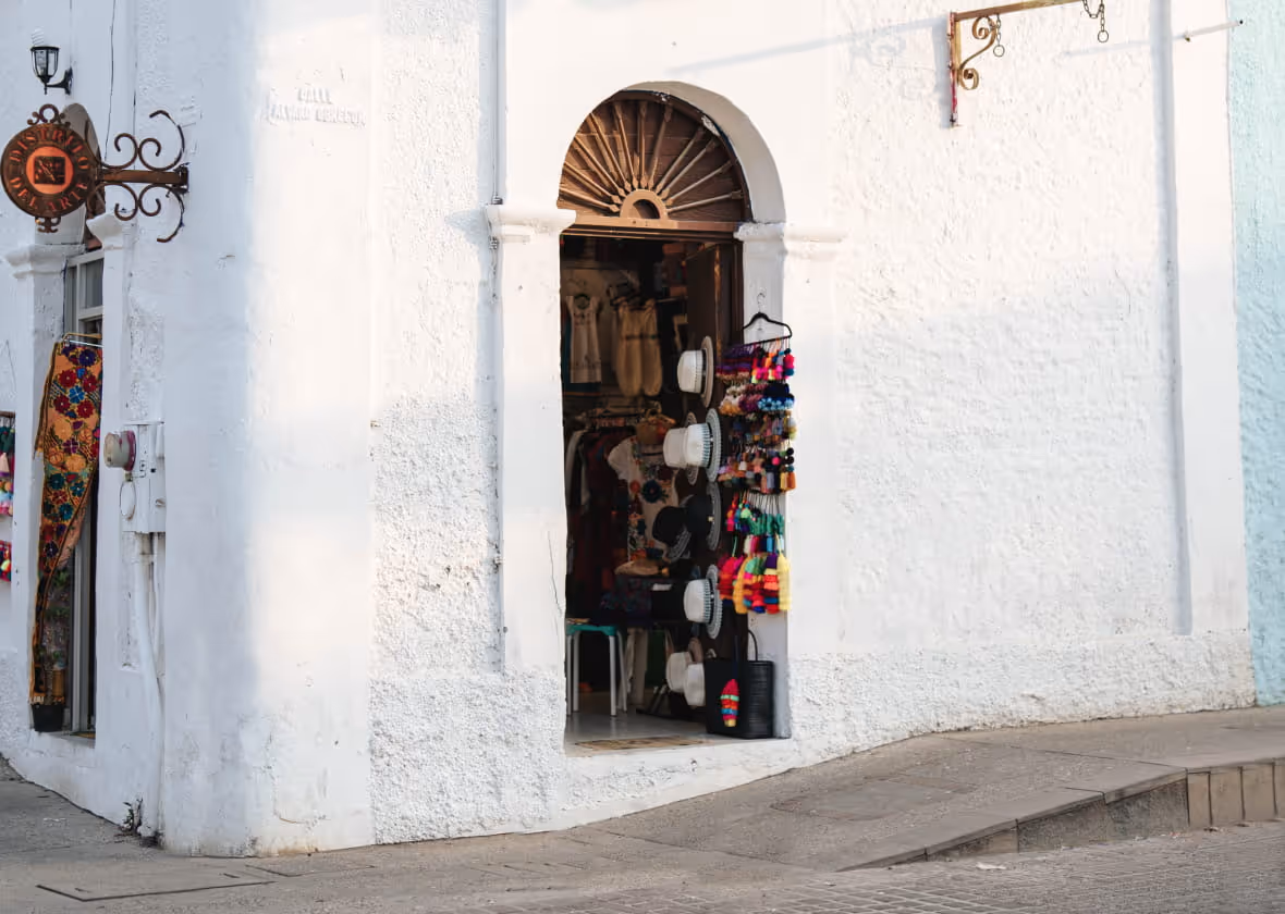White-walled Mexican souvenir shop on Calle Alvaro Obregon with hats, colorful pom-poms, and an arched doorway