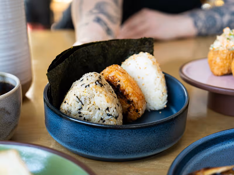 Three Japanese onigiri rice balls with different fillings nestled in nori seaweed inside a blue ceramic bowl