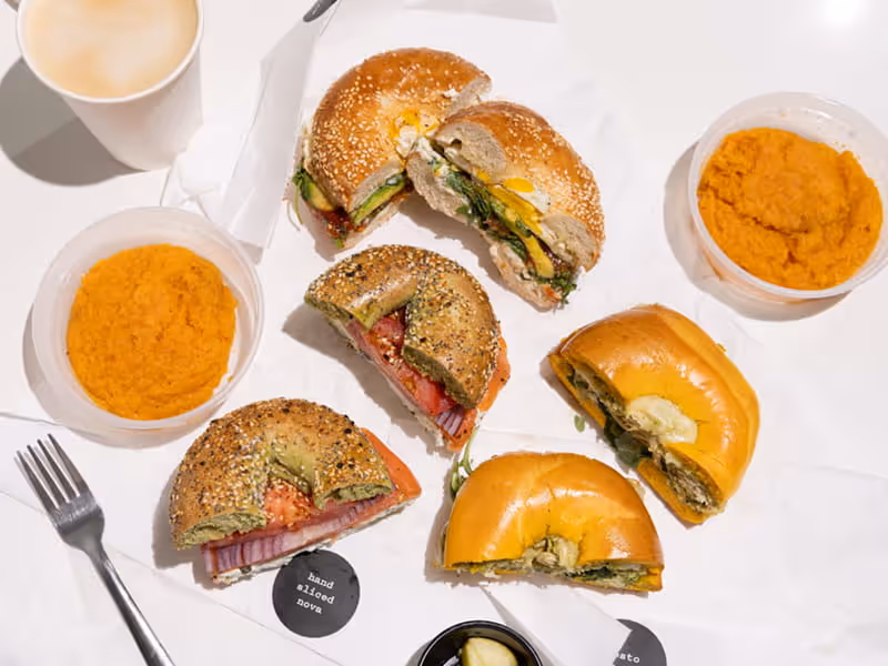 Assorted bagel sandwiches cut in half with pesto, vegetables, and smoked nova alongside containers of carrot spread.