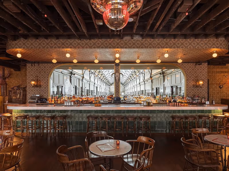 Elegant vintage-style cocktail bar with a large mirror, extensive liquor selection, disco ball, patterned wallpaper