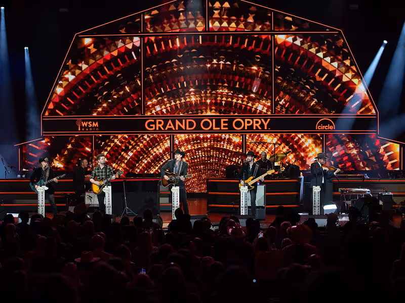 Country music band performing live on the Grand Ole Opry stage with WSM Radio and Circle logos illuminated behind them.