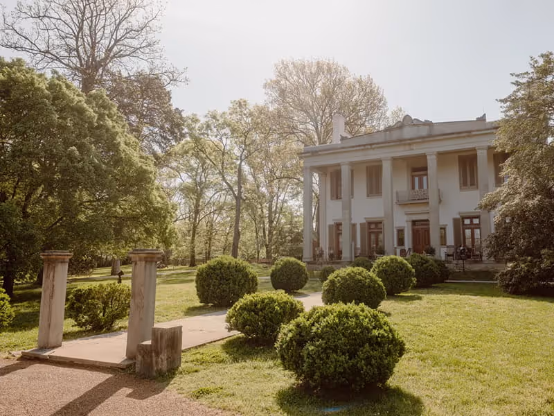 White Greek Revival mansion with tall columns and manicured boxwood shrubs on a lush green lawn in Nashville, Tennessee.