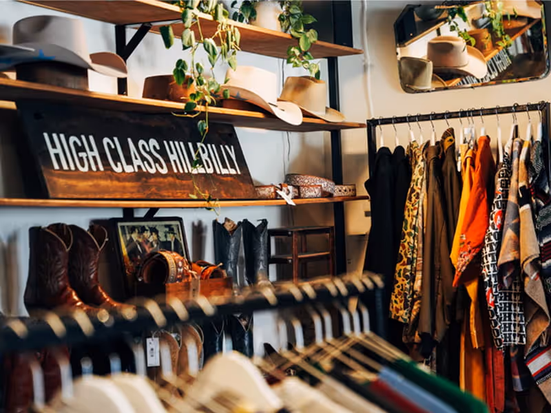 Vintage western shop displaying cowboy boots, hats, belts, and clothing on racks beneath a High Class Hillbilly sign.