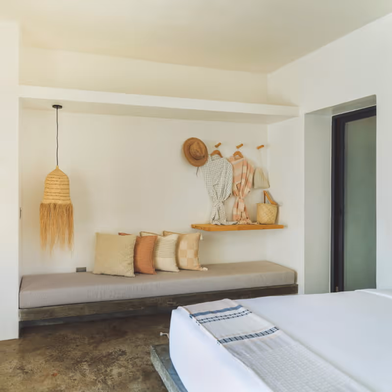 Minimalist boutique hotel bedroom with a built-in daybed, decorative pillows, woven pendant lamp, and wall hooks