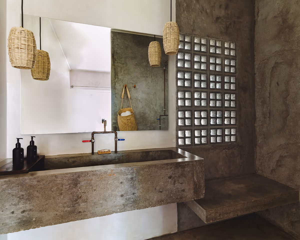 Industrial-style bathroom with a concrete trough sink, woven pendant lights, glass block wall, and a large wall mirror