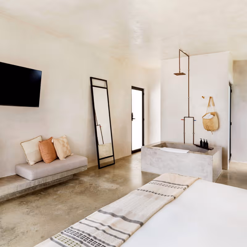 Boutique hotel room with concrete bathtub, copper rainfall shower, wall-mounted TV, full-length mirror, and a daybed