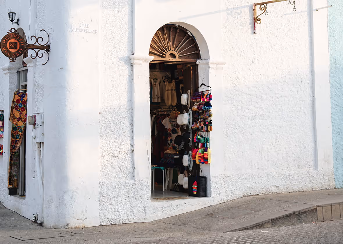 White-walled Mexican artisan shop on Calle Alvaro Obregon displaying colorful hats, tassels, and handcrafted souvenirs