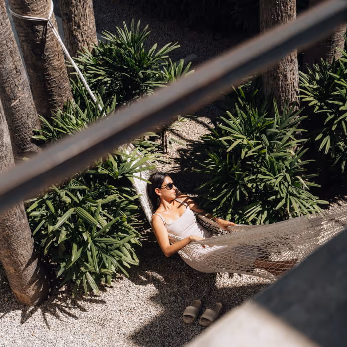 Woman in white outfit relaxing in a hammock surrounded by tropical plants and palm trees, viewed from above