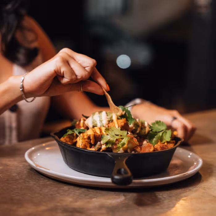 Hands scooping food from a cast iron skillet dish garnished with cilantro and drizzled sauces on a white plate