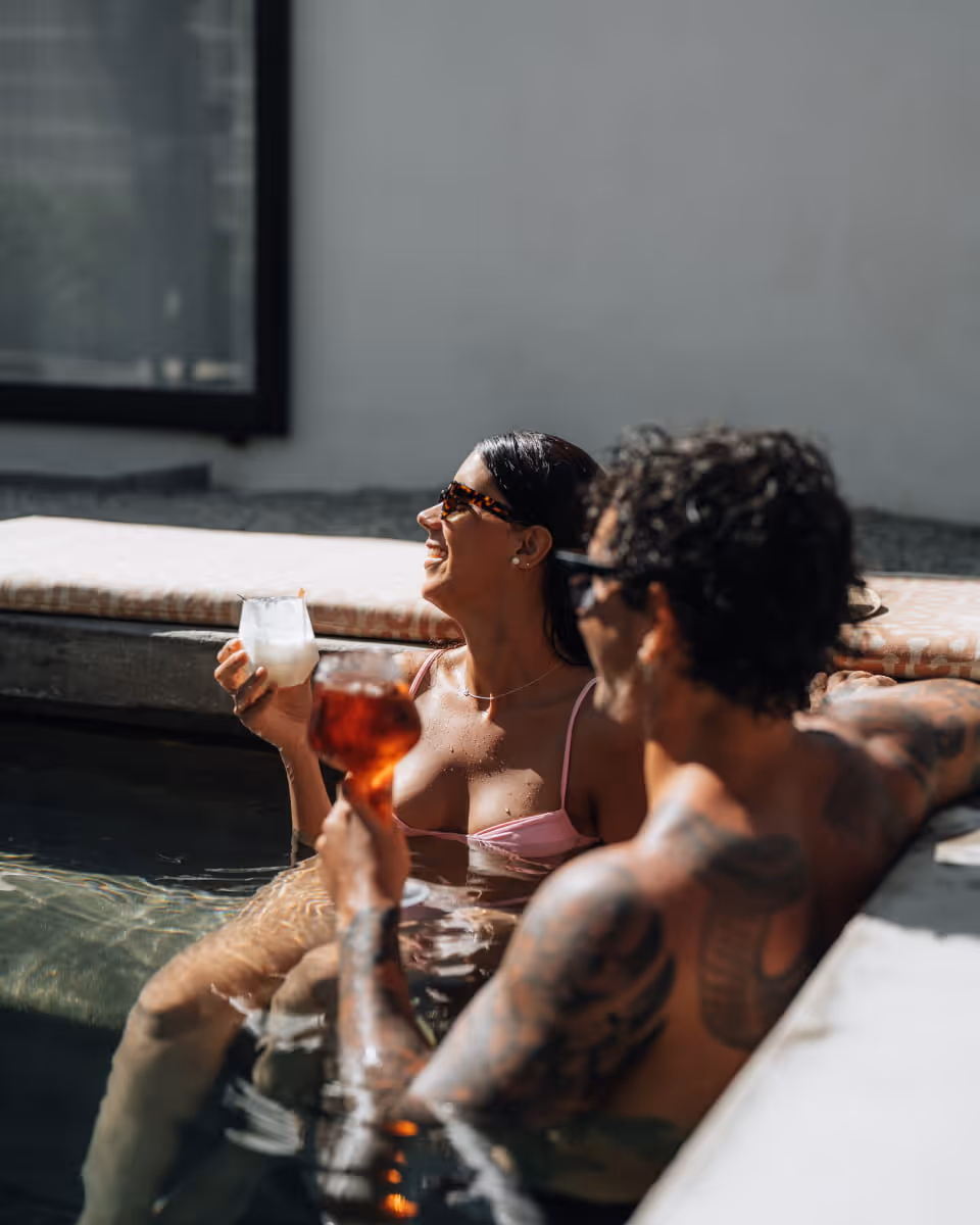 A couple relaxing in a pool with cocktails, smiling and enjoying the sun at a boutique hotel or resort