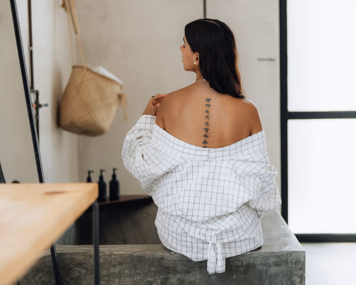 Woman with dark hair sitting with her back exposed, revealing a vertical Chinese character tattoo along her spine.
