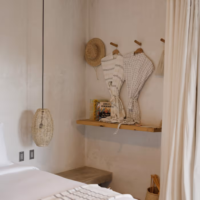 Minimalist rustic bedroom with woven pendant light, straw hat, and linen robes hanging on wooden wall hooks