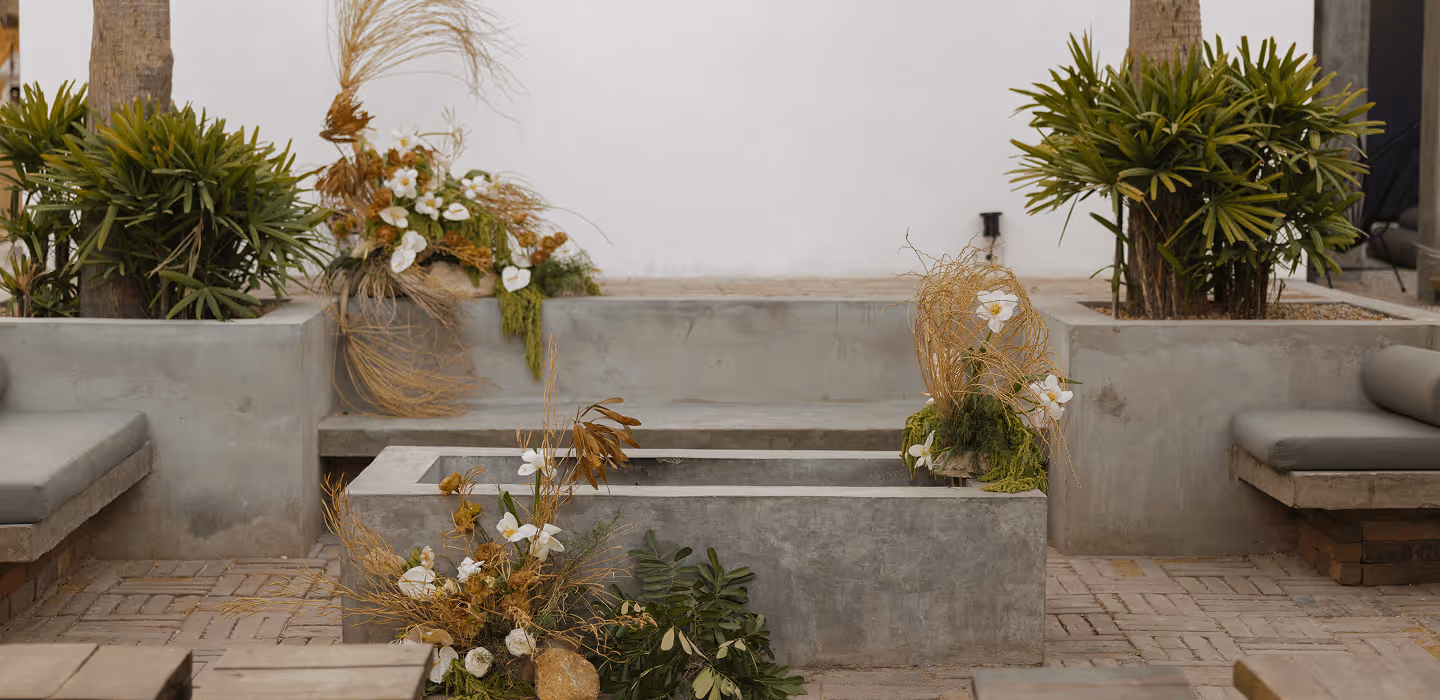 Concrete outdoor seating area with herringbone brick flooring, decorated with white orchids, dried grasses, and lush