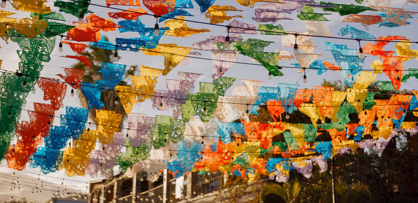 Colorful papel picado banners with skull designs strung across an outdoor space with string lights for a Mexican celebration