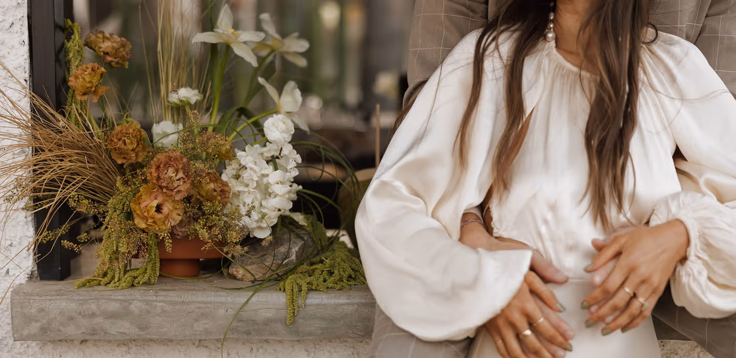 Couple sitting beside an elegant floral arrangement with amber roses, white hydrangeas, and dried grasses at an intimate