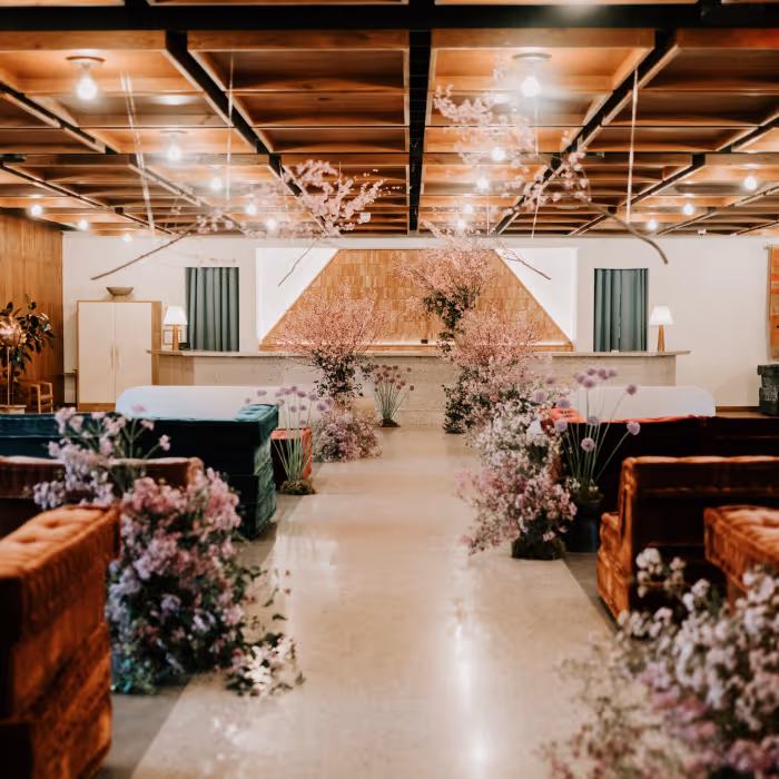 Stunning wedding ceremony aisle lined with pink cherry blossoms and lavender floral arrangements between velvet lounge