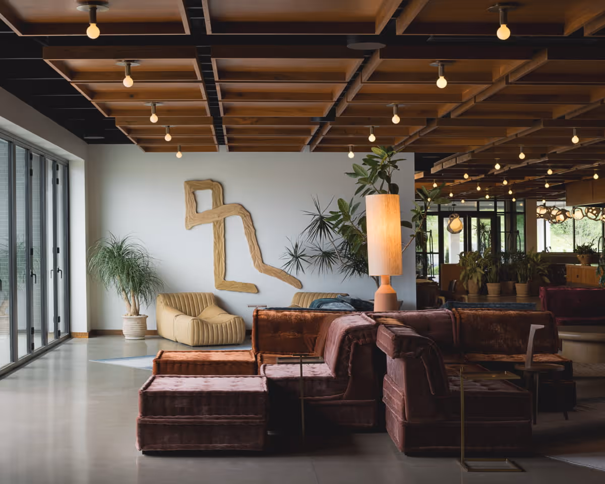 Stylish hotel lobby with plush velvet modular sofas, abstract wooden wall sculpture, indoor plants, warm wood ceiling