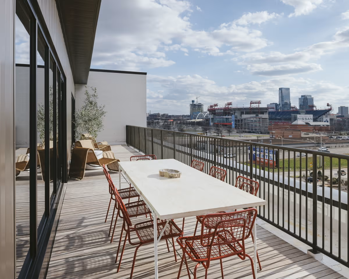 Rooftop balcony with a dining table and red metal chairs overlooking Nissan Stadium and the Nashville skyline on a partly