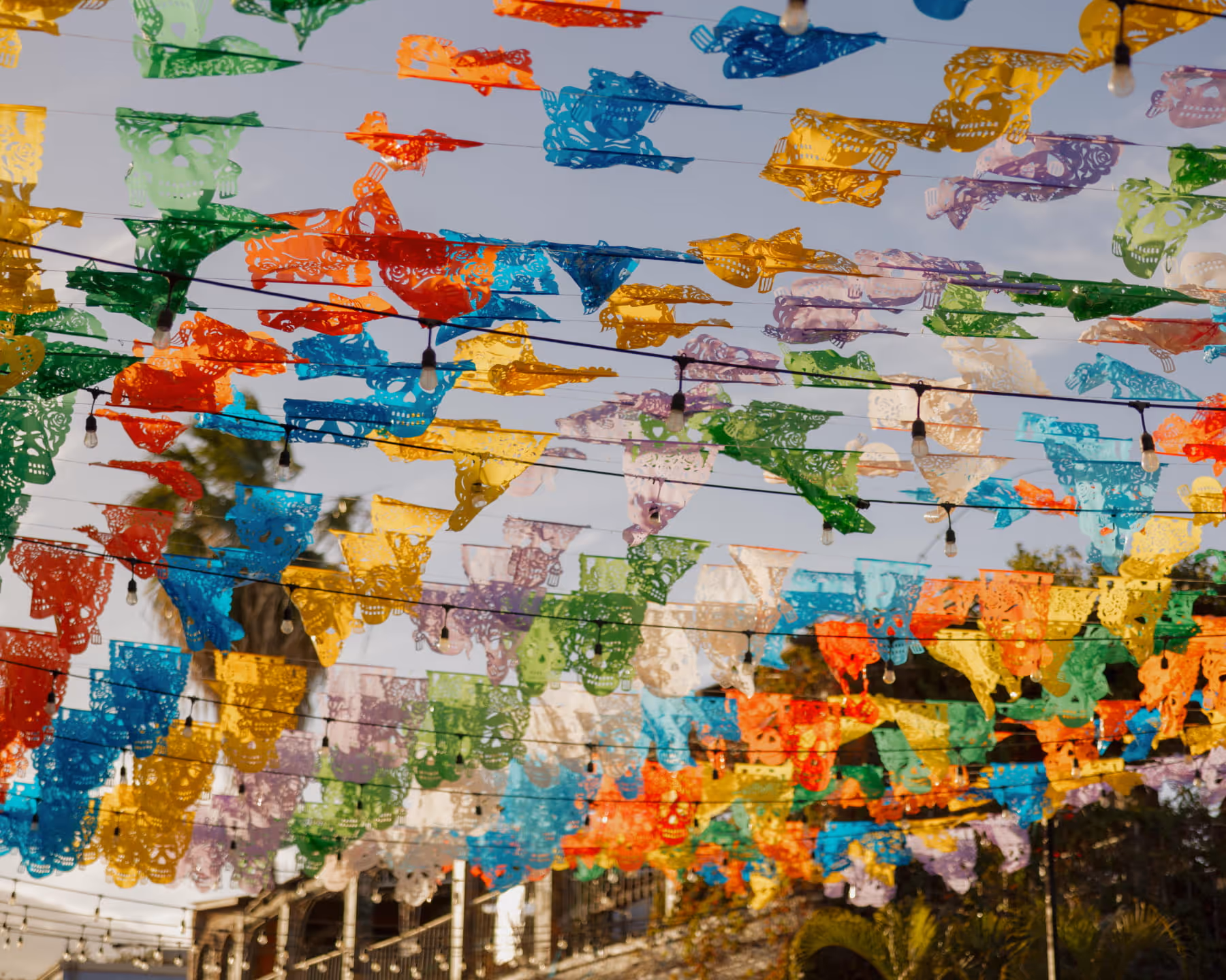 Colorful papel picado banners with skull designs strung across an outdoor space with string lights for a Mexican celebration