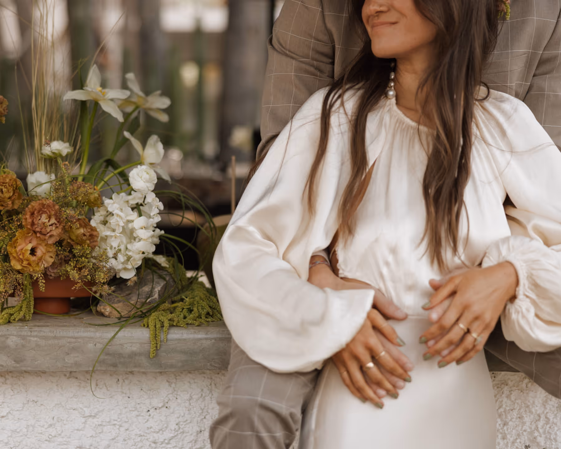 Couple sitting beside an elegant floral arrangement with amber roses, white hydrangeas, and dried grasses at an intimate