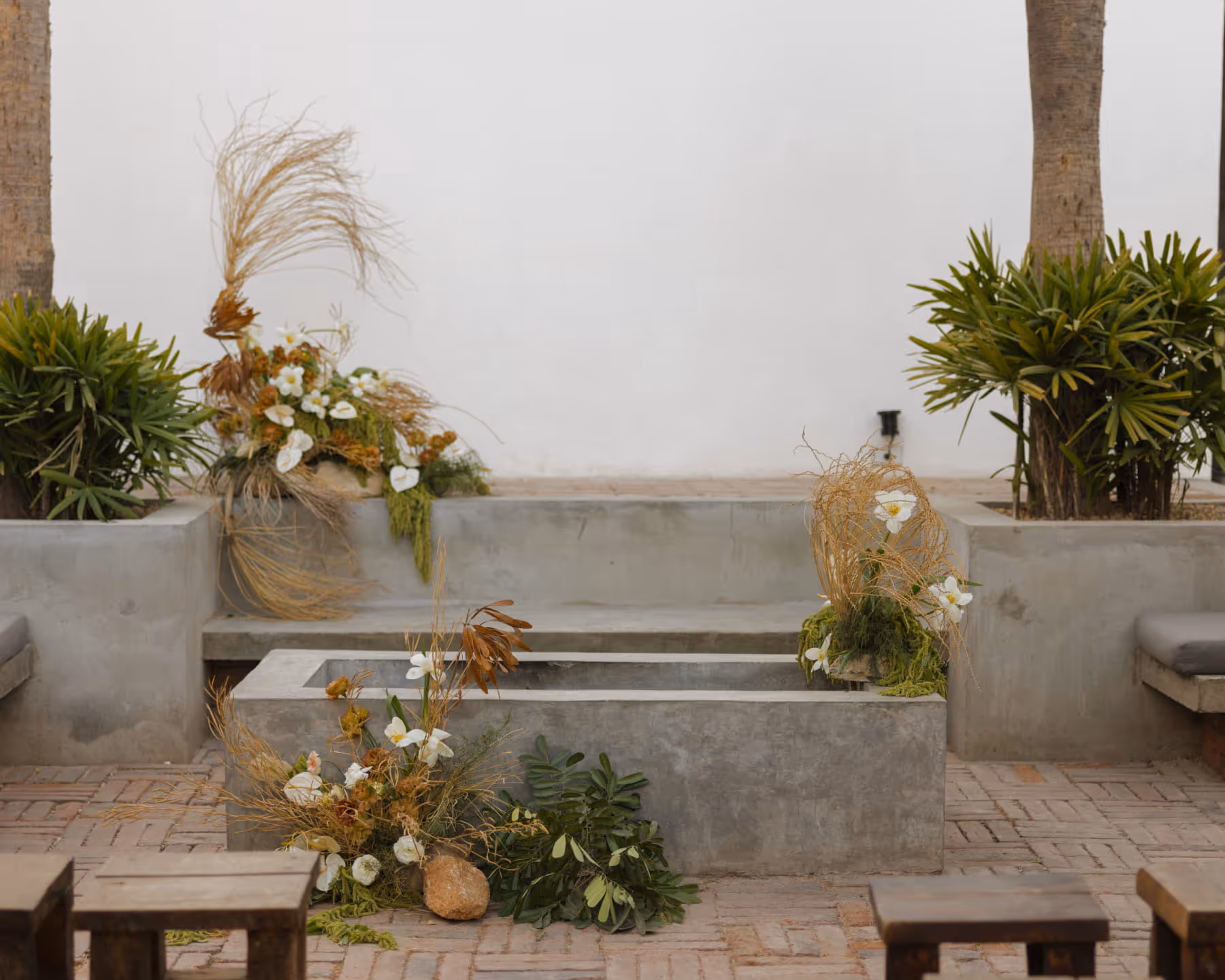 Concrete outdoor seating area with herringbone brick flooring, decorated with white orchids, dried grasses, and lush