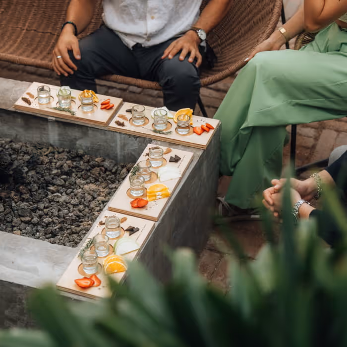 Mezcal or tequila tasting flight boards arranged around a fire pit, each with small glasses, fruit, and garnishes