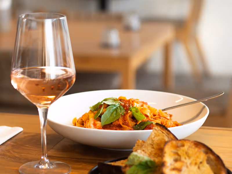 Glass of rose wine alongside a plated Italian pasta dish at Come a Casa restaurant