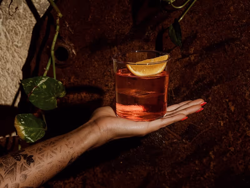 Crafted cocktail with citrus garnish at Neat by Lumbre lounge in a moody, intimate setting