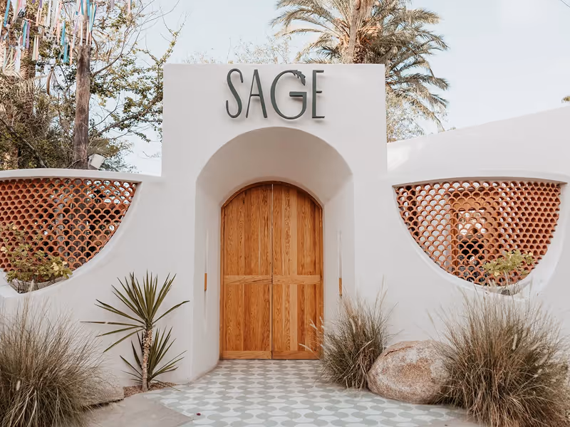 Entrance to Sage Baja restaurant with arched white facade and lush greenery in San Jose del Cabo