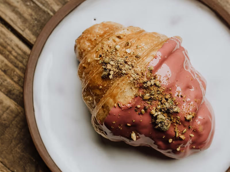 Fresh croissant topped with prosciutto served on a white plate at Ruba's Bakery and Bistro