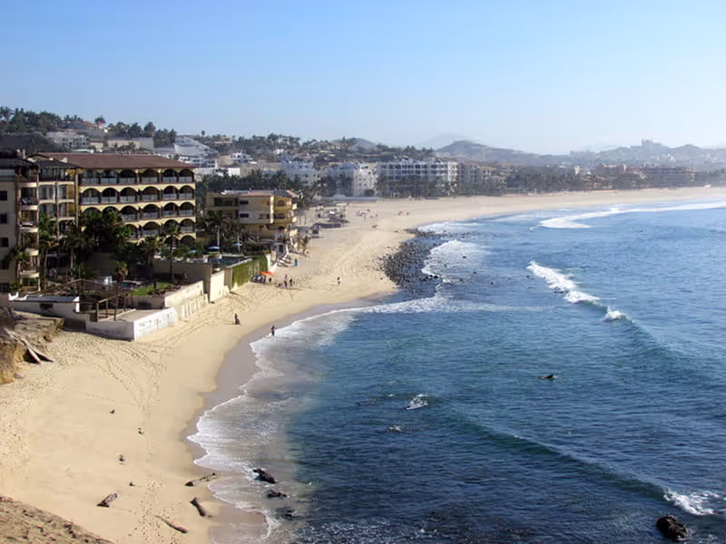 Aerial view of Costa Azul Beach with surfers in the water and coastal mountains in the distance