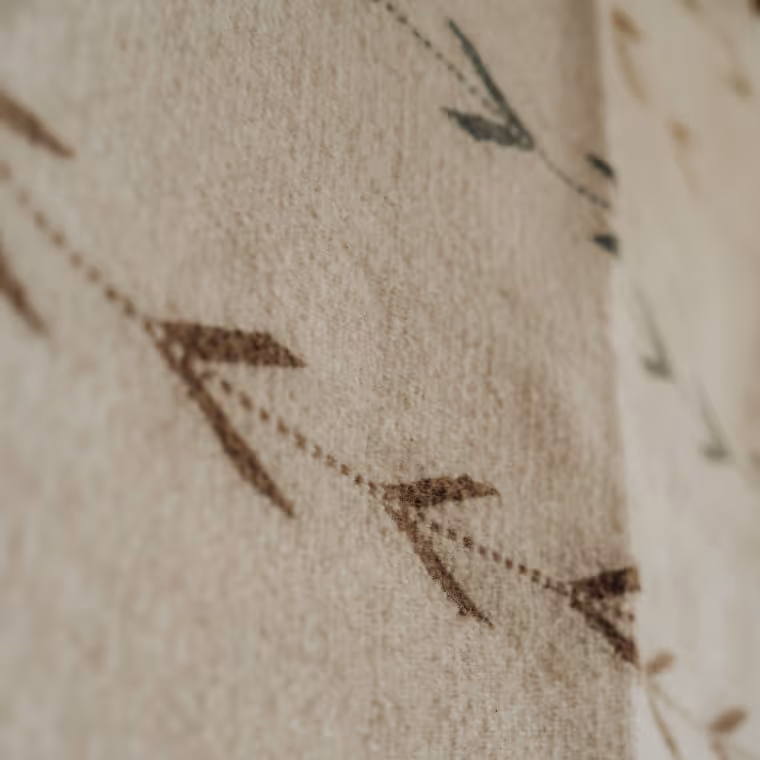 Close-up of a soft woven textile with brown and green arrow-shaped patterns on a cream-colored wool blanket