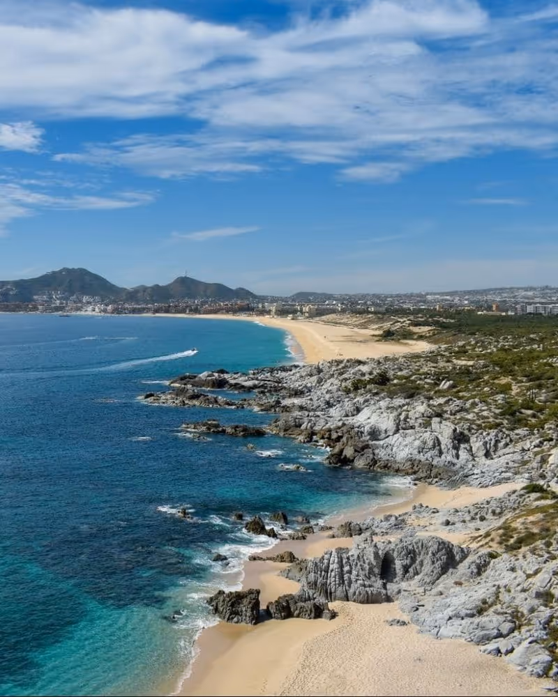 Stunning aerial view of Cabo San Lucas coastline with turquoise waters, rocky shores, sandy beaches, and distant mountains