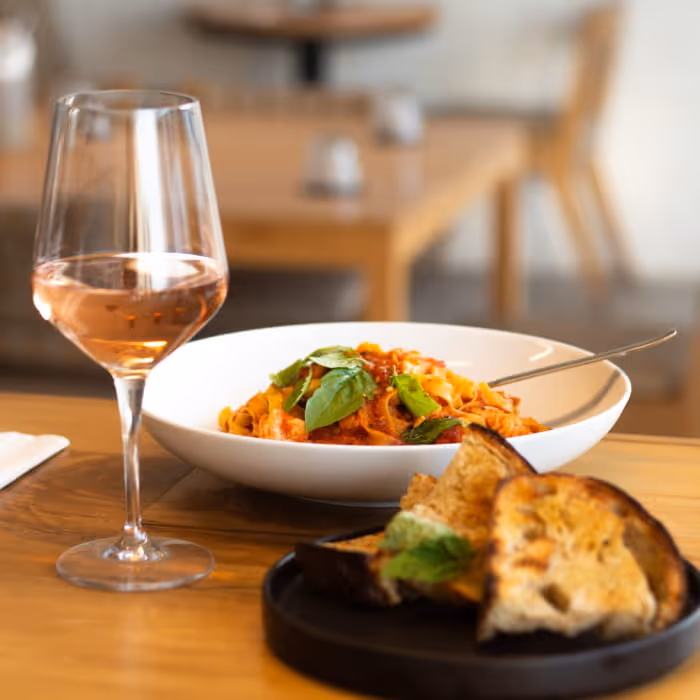 A bowl of fresh tagliatelle pasta in tomato sauce with basil, served alongside grilled bread and a glass of rosé wine.