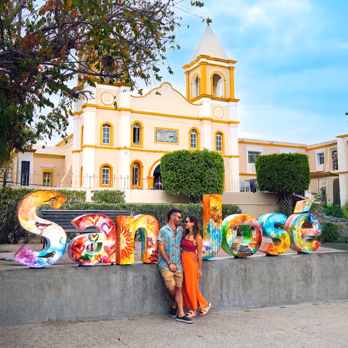 Couple posing in front of the colorful San José sign and historic mission church in San José del Cabo, Mexico