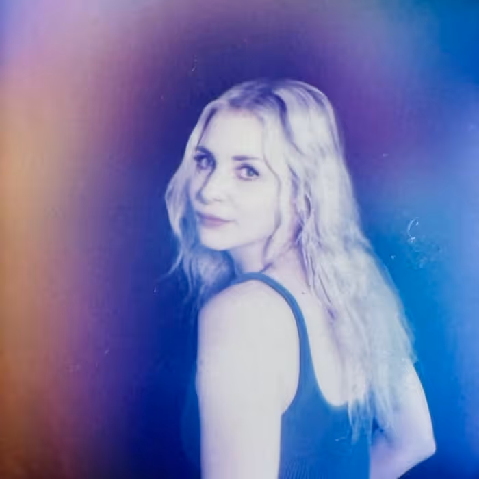 Young woman with blonde wavy hair looking over her shoulder, photographed with a dreamy purple and blue aura glow effect.