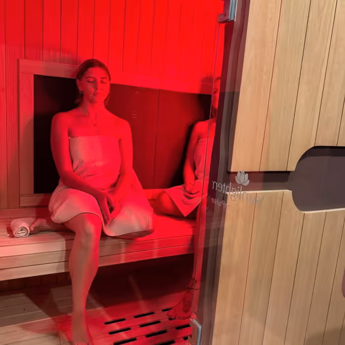 Woman relaxing in an infrared sauna cabin bathed in red light at a wellness spa facility