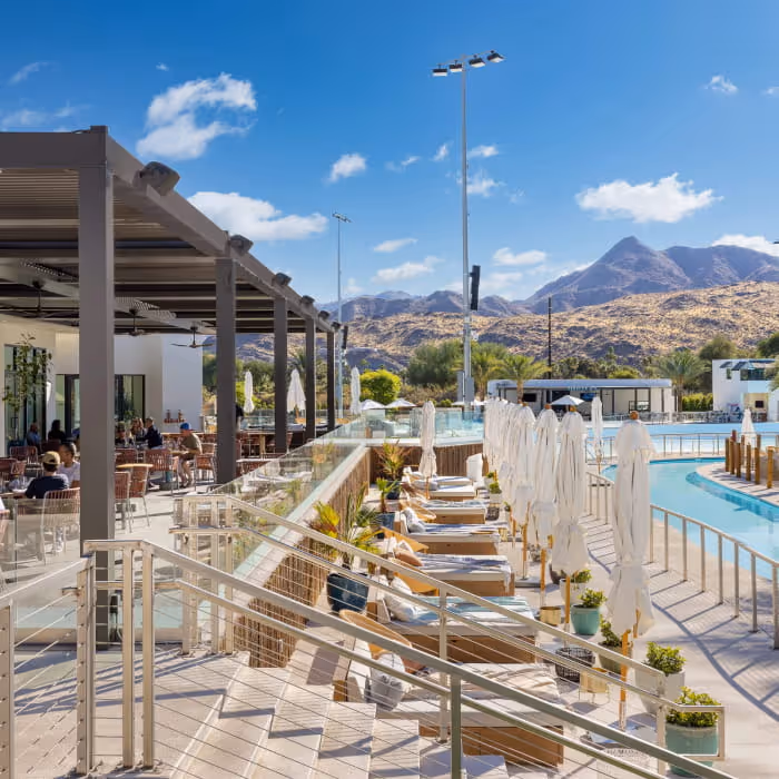 Desert resort pool deck with lounge chairs, umbrellas, and a covered dining area against rugged mountain scenery