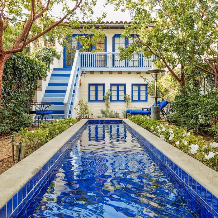 Charming blue-and-white Mediterranean-style home with an exterior staircase and a narrow blue-tiled lap pool surrounded