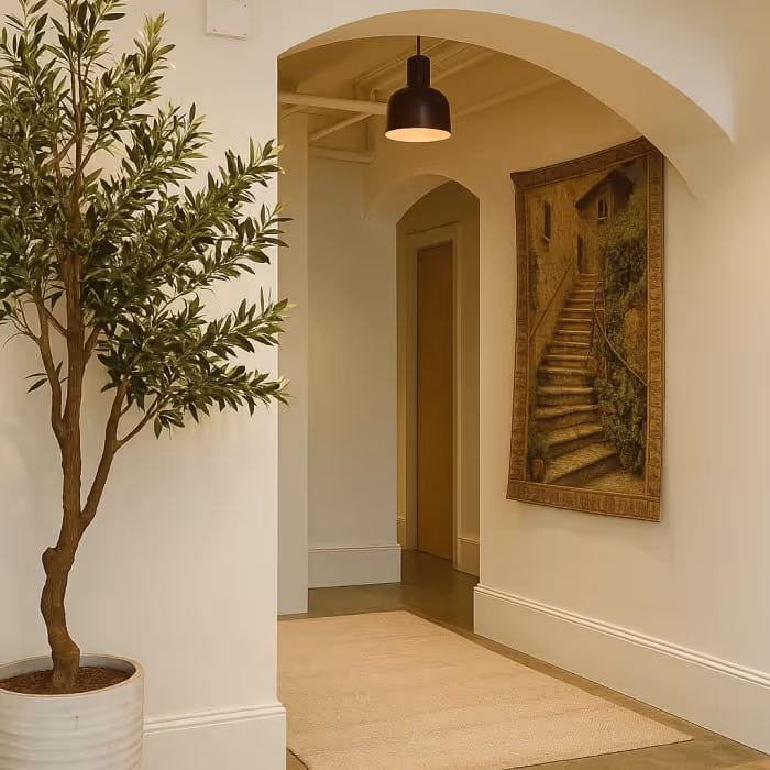 Elegant hallway with arched doorways featuring a potted olive tree, pendant light, and a tapestry of stone stairs.