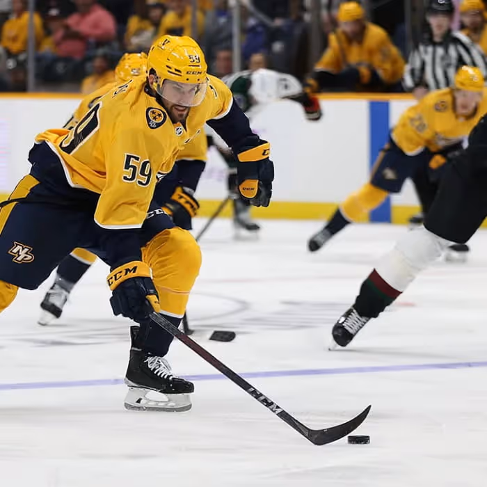 Nashville Predators hockey player number 59 skates with the puck during an NHL game against a green-uniformed opponent.