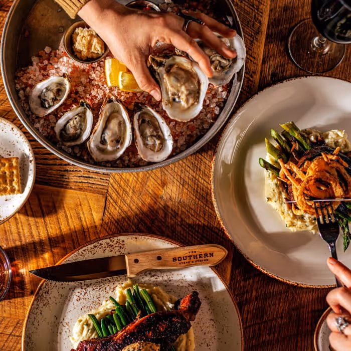 Overhead view of a dinner spread at The Southern Steak & Oyster featuring fresh oysters on ice, grilled steak, and asparagus.