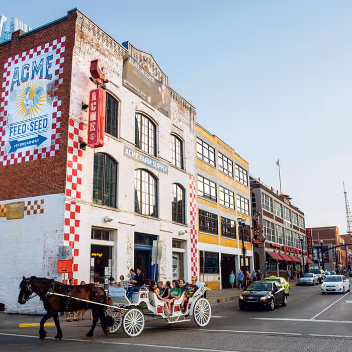 Horse-drawn carriage passes the Acme Feed & Seed building on Broadway in Nashville, Tennessee, on a sunny day.
